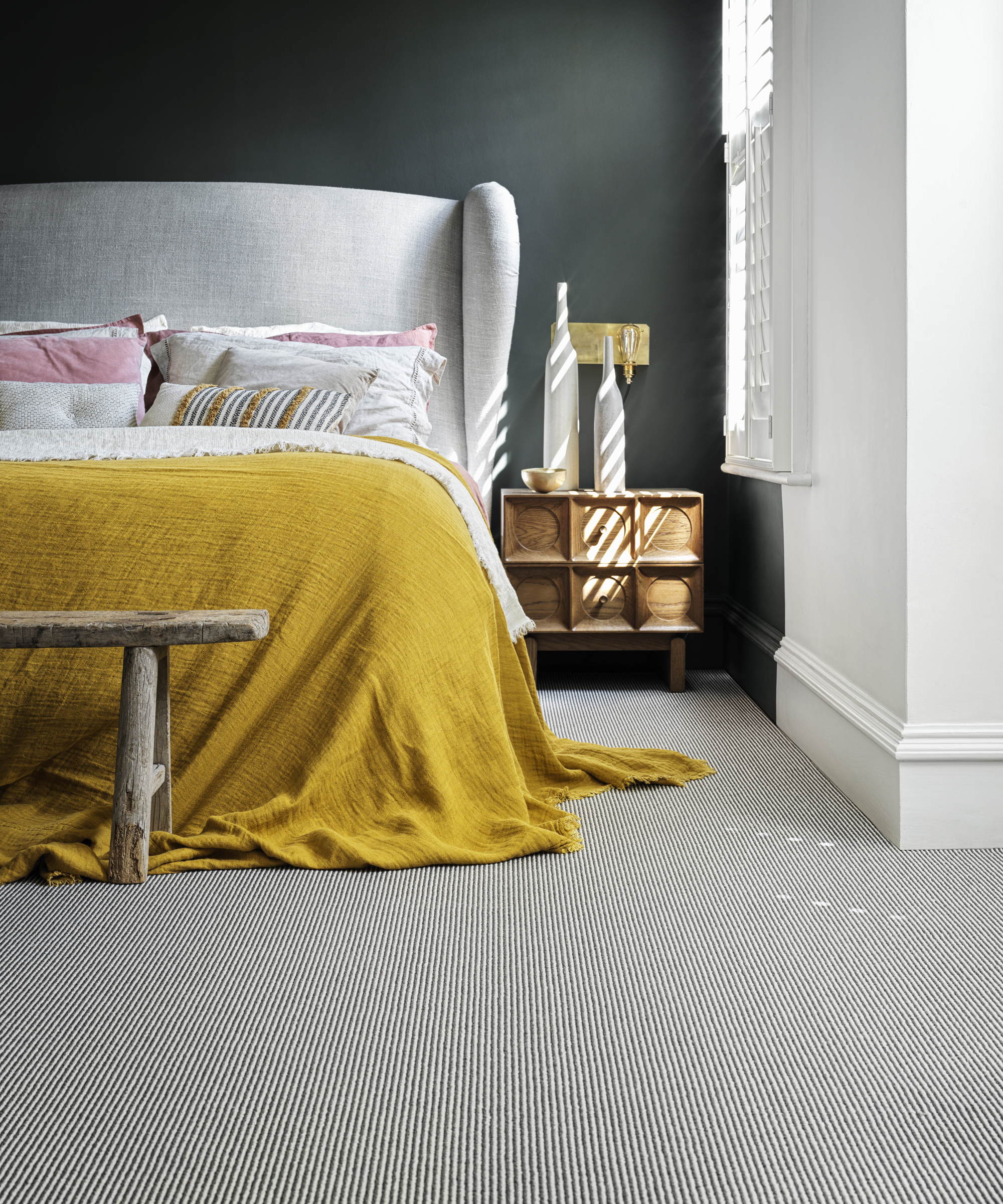 A bedroom with black walls, a white bed with yellow throw, and black and white striped carpet