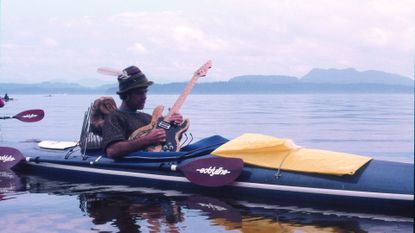 Jim Nollman playing electric guitar in a modified kayak.
