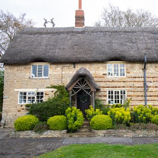 thatched cottage with wooden front porch and golden brown bricks