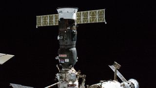 a dark-gray spacecraft docks to the international space station with the blackness of space in the background.