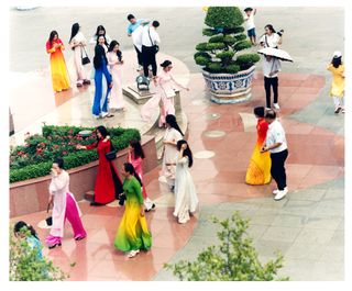Above, a group of visitors in front of the Ho Chi Minh Museum, after taking photographs next to a statue representing Ho Chi Minh as a young man. The women are wearing colourful ao dai outfits, a Vietnamese garment consisting of a long split tunic worn over trousers