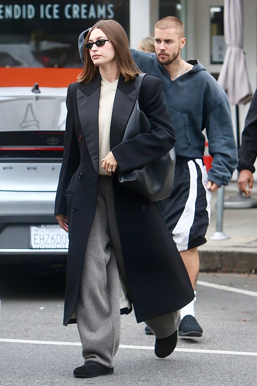 Hailey Bieber wearing a black coat with sweatpants and Ugg Elea slides