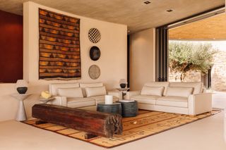 A neutral living room with rustic patterned rug and wall hanging