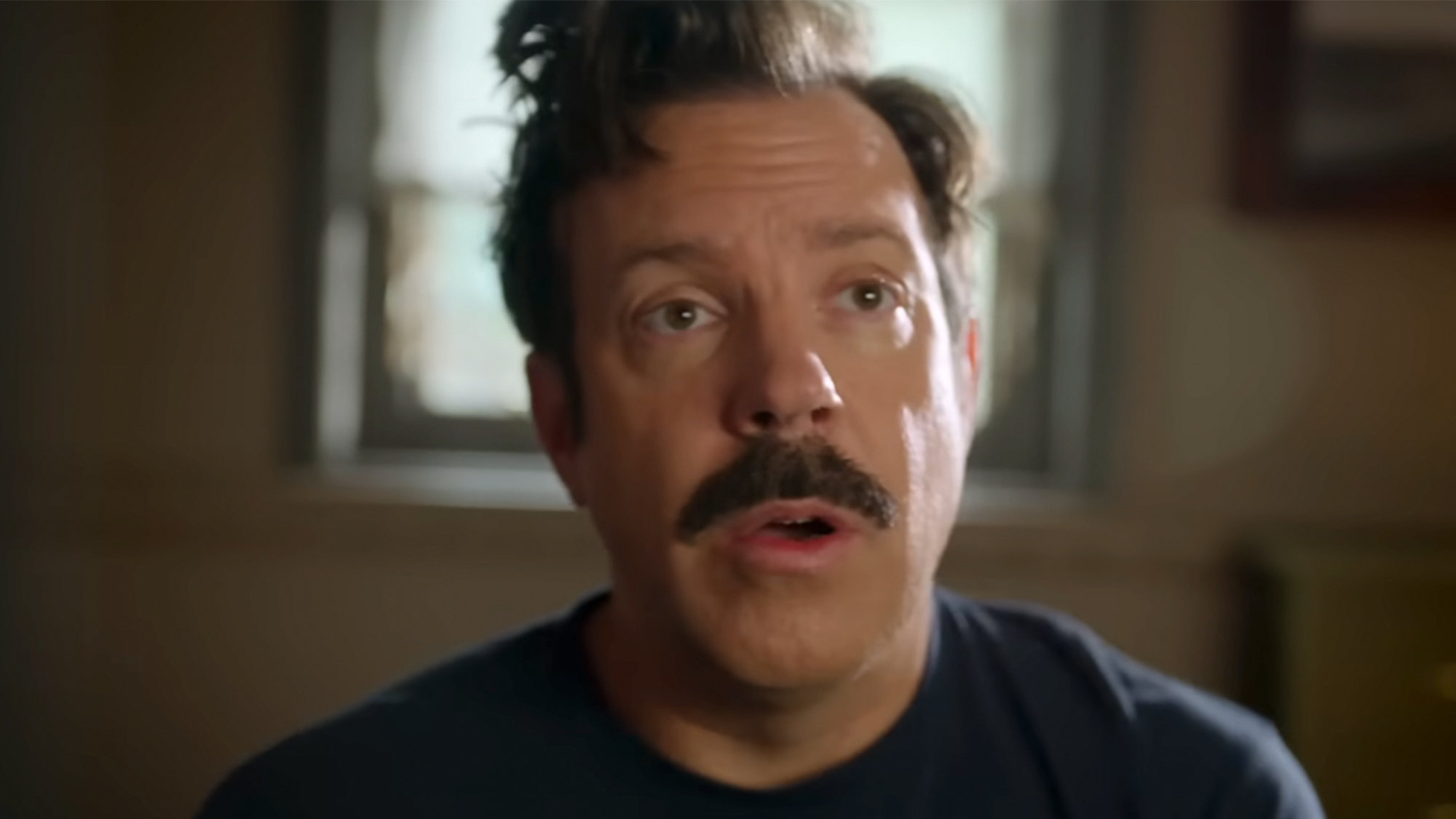 Jason Sudeikis with messed up hair looking out of it in Ted Lasso