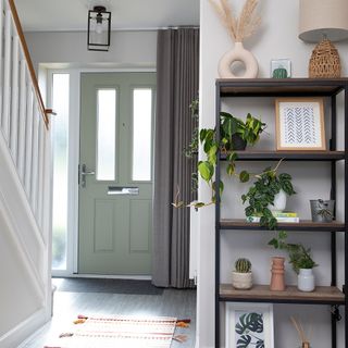 white hallway entrance with green front door industrial shelving unit table lamp round vase rug runner white painted staircase