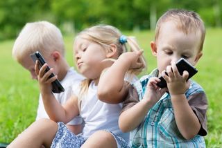 Happy children using smartphones sitting on the grass. 