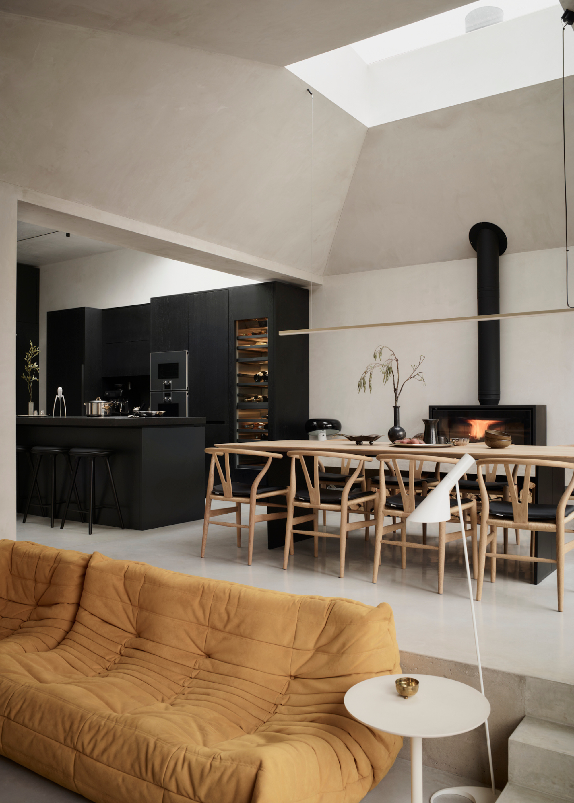 sleek all black kitchen cabinetry in an open plan living space with a modern dining table and yellow togo sofa
