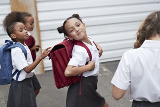 kids in school uniforms smiling at camera while walking to school wearing their backpacks