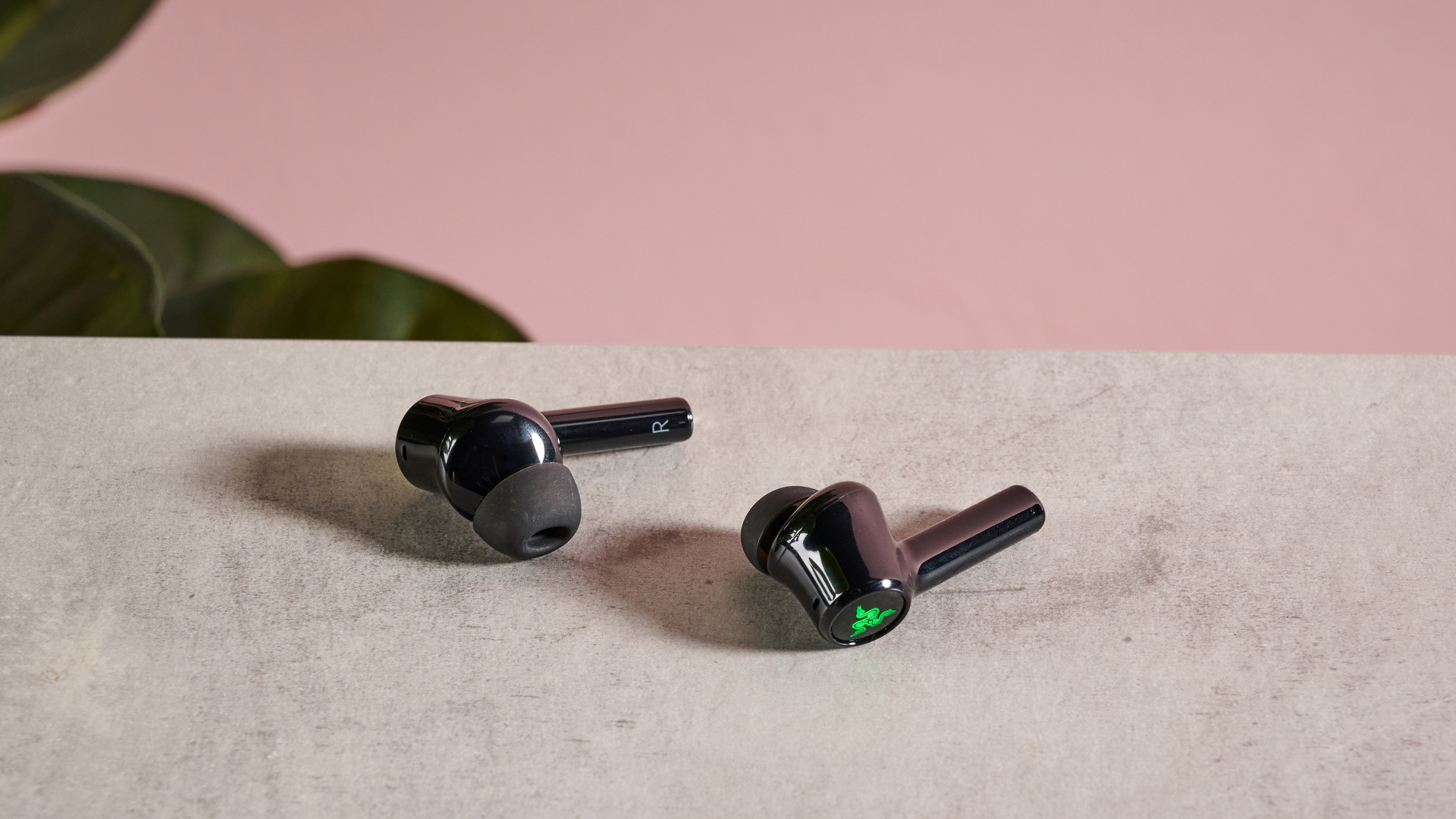 Razer Hammerhead Pro HyperSpeed earbuds on table with pink and plant in background