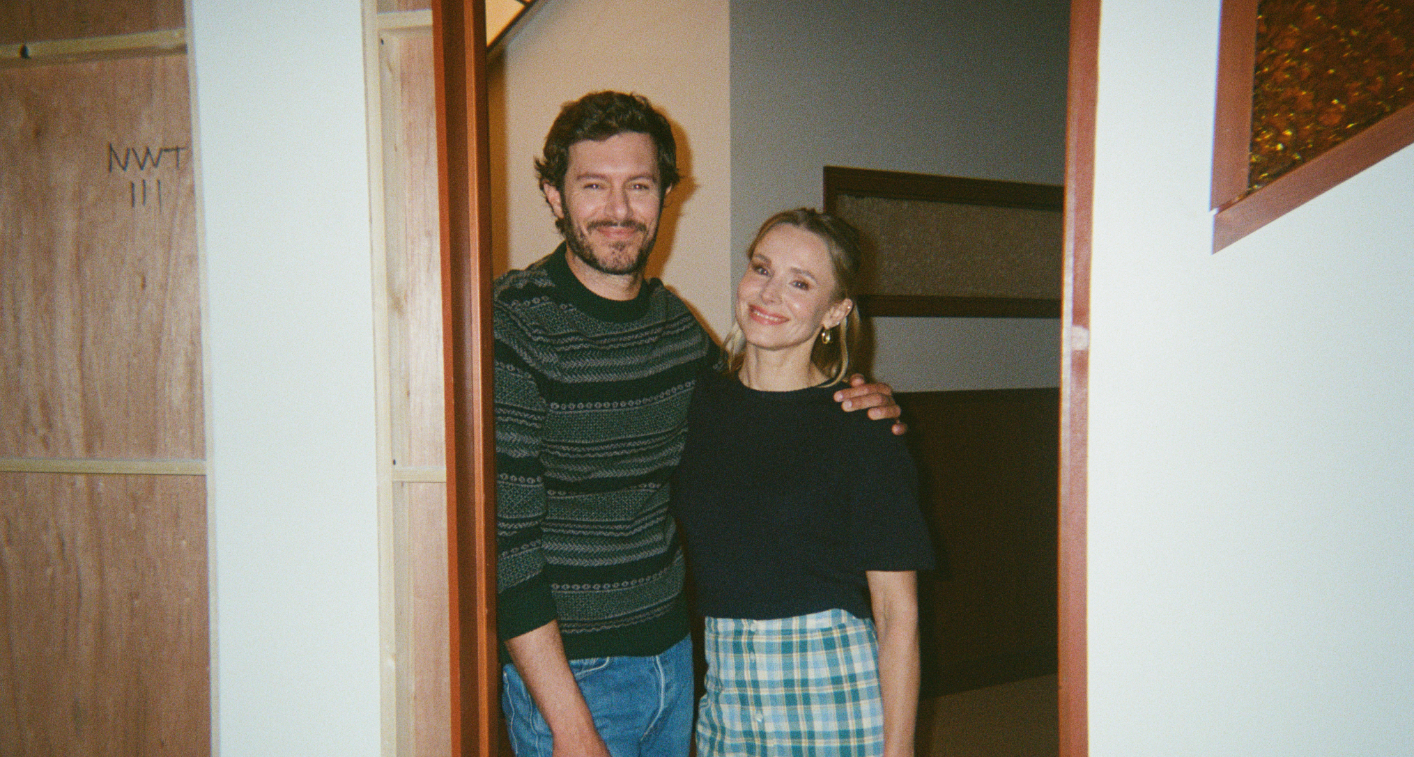 nobody wants this stars adam brody and kristen bell pose together smiling while standing in a doorway on set of the netflix show