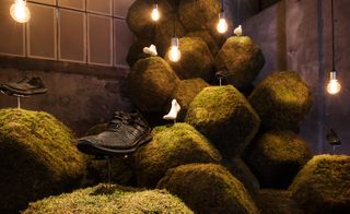 View of a 'The Nature Of Motion’ installation featuring grass covered 3D hexagons, exposed bulb pendant lights, the NikeLab Free RN Motion Flyknit shoe and mannequin feet