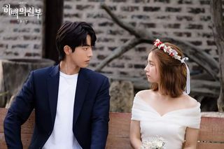 a man in a blazer and a woman in a wedding dress and flower crown look at each other while sitting on a bench, in the korean drama 'the bride of habaek'