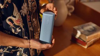 A blue Sonos Roam 2 portable speaker held by a man wearing a Hawaiian shirt