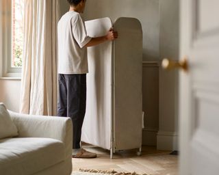 A man next to the Eclipse™ 3-tier Ecru Clothes Drying Rack With Screen in a bright living room