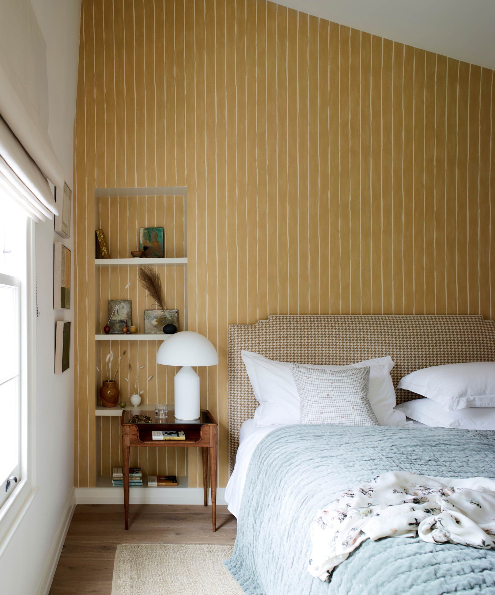 a bedroom with a striped yellow wall, a small side table, and a bed with a blue quilt on it