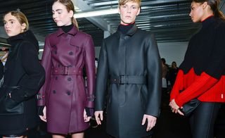 Four models - one with a black duffel coat, one with a purple trench coat, one with a black trench coat and one in a red and black jumper