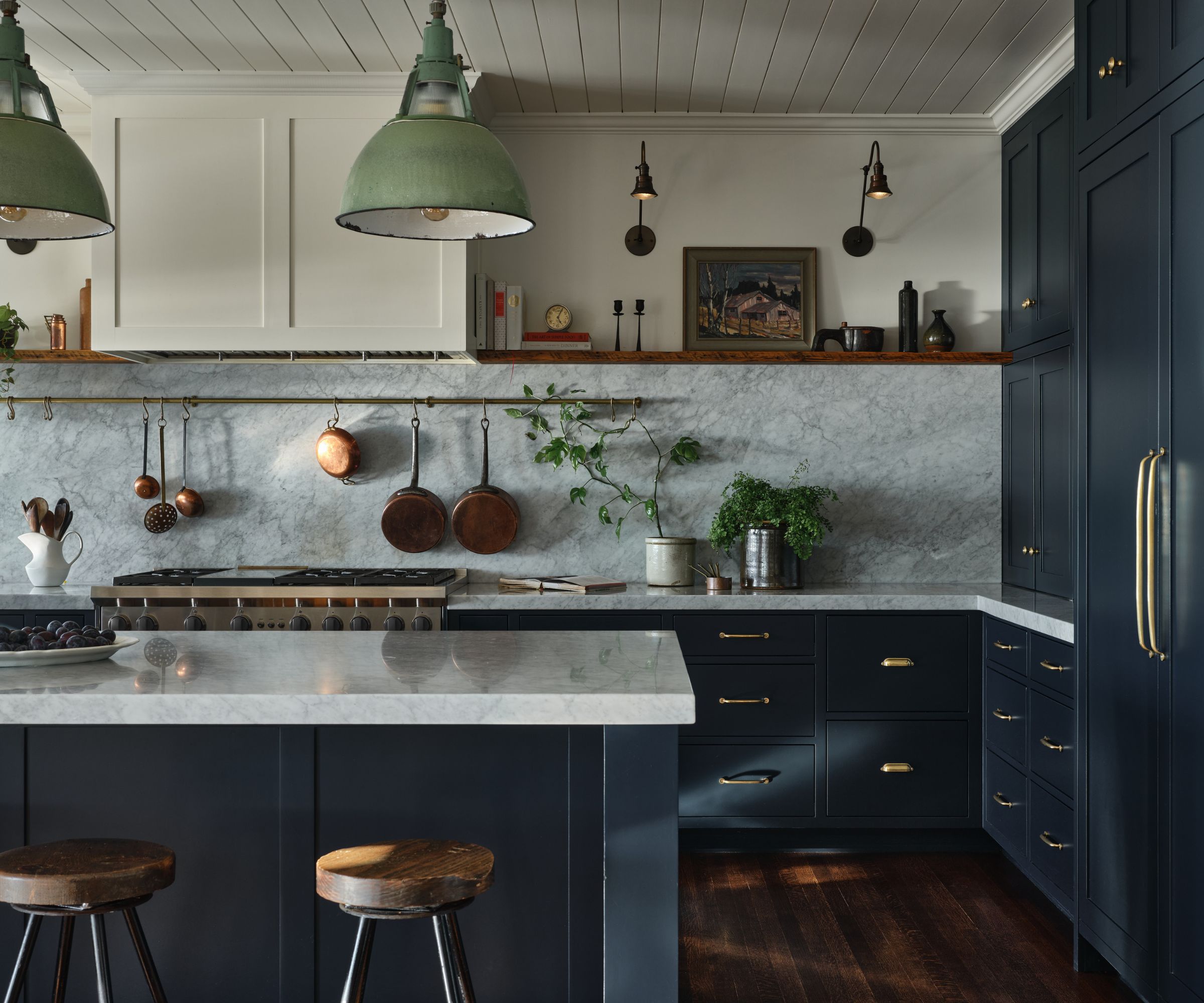 A Craftsman kitchen with dark blue cabinets, marble countertops, and a brass pot hanger on the marble backsplash