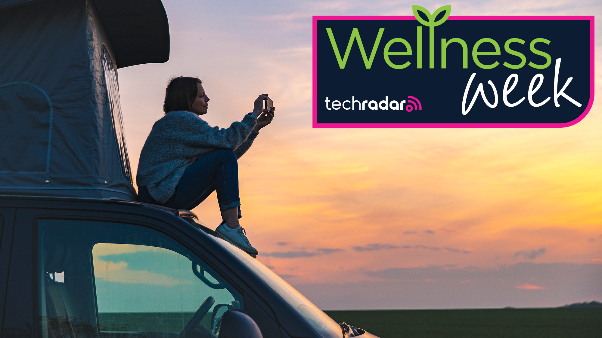 Woman sat on a tented van, phone in hand, to take a picture off the sunset. A adge reading "Wellness Week, TechRadar" is overlaid.