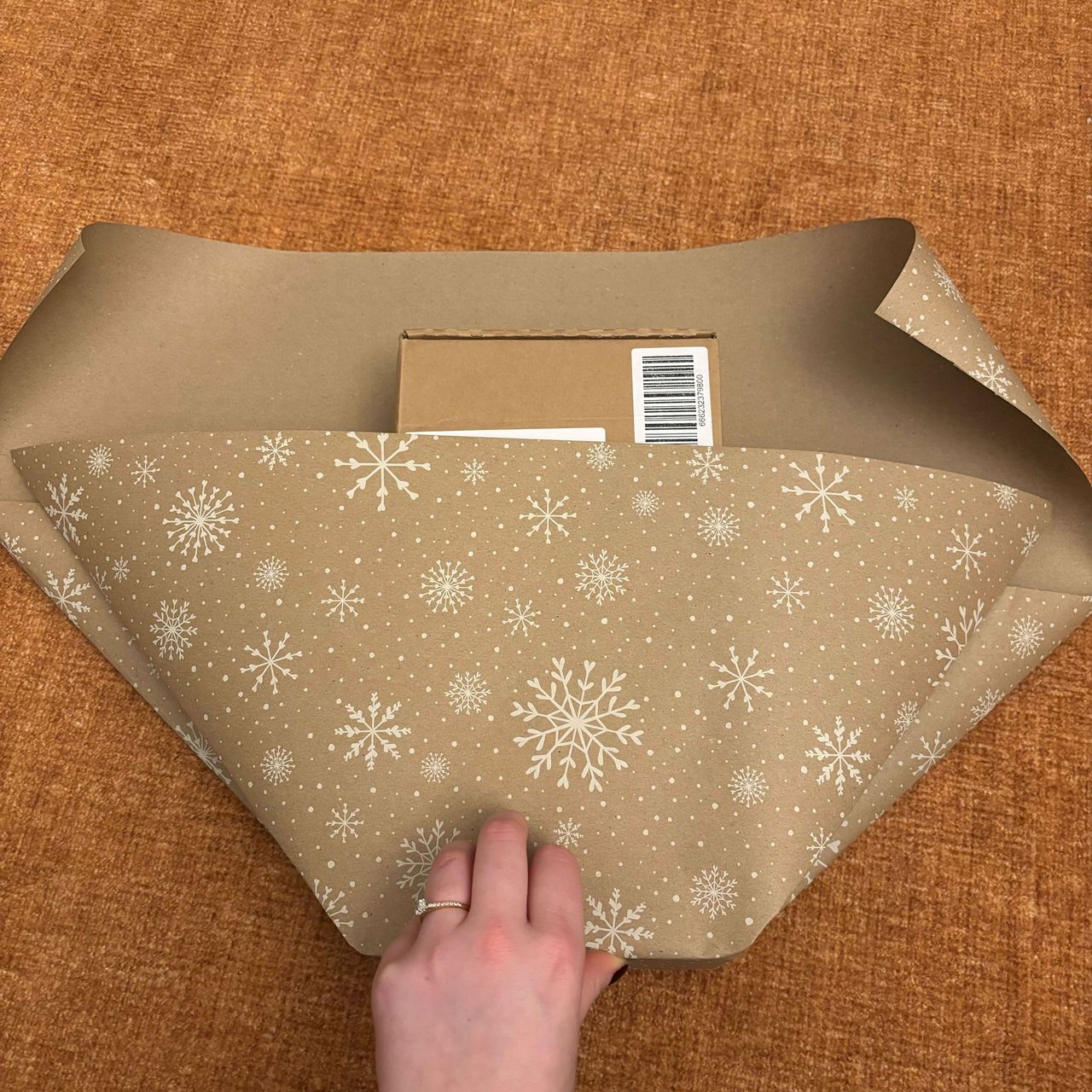 A rectangular box wrapped in brown paper with a white snowflake print on it