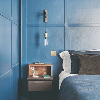 Navy blue wood panelling walls with bed, blue bedding and wooden bedside table