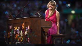 Taylor Swift onstage at Wembley Stadium on June 23, 2024. She is behind a piano painted with flowers and is wearing a pink dress