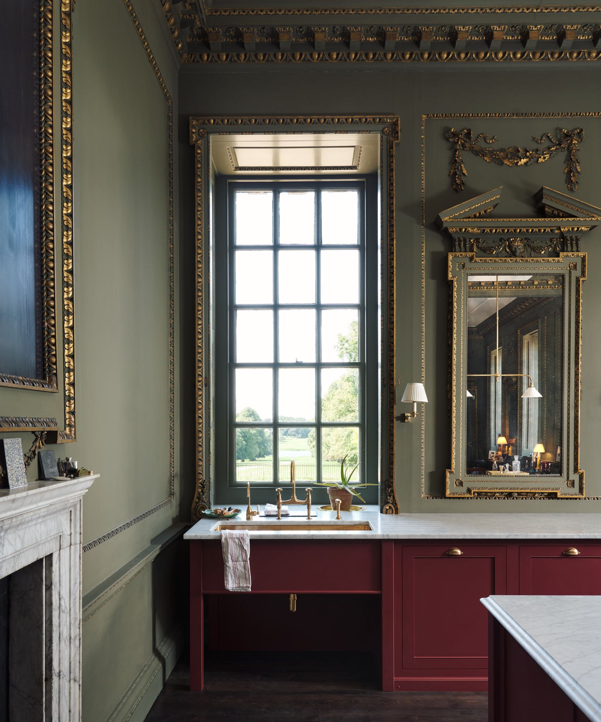 A stately home kitchen with green walls, red cabinets, marble countertops, and mirrors on the walls