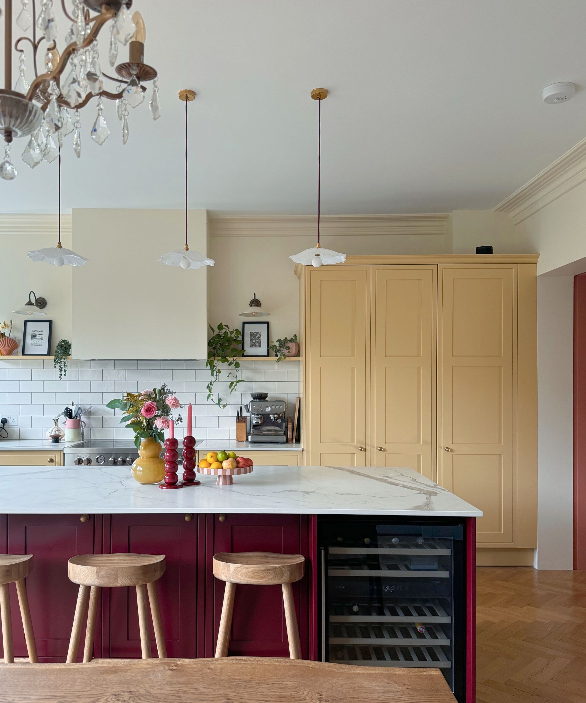 Kitchen with high ceiling, parquet flooring, a red island with a marble countertop, butter yellow painted cabinetry, and a white tiled backsplash.