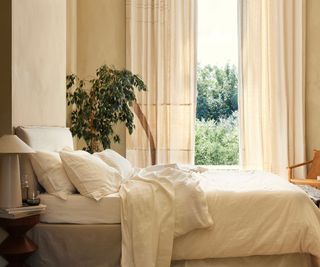 Side view of white bedding on a bed against white walls and an open window.