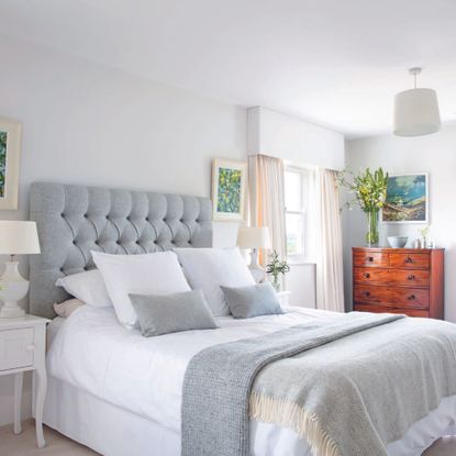 farmhouse bedroom with neutral colour scheme grey upholstered bed with white linen and brown wood dresser against wall1