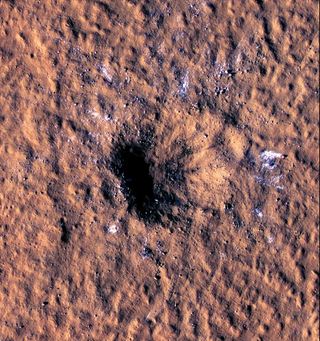 a deep crater on a dusty red surface
