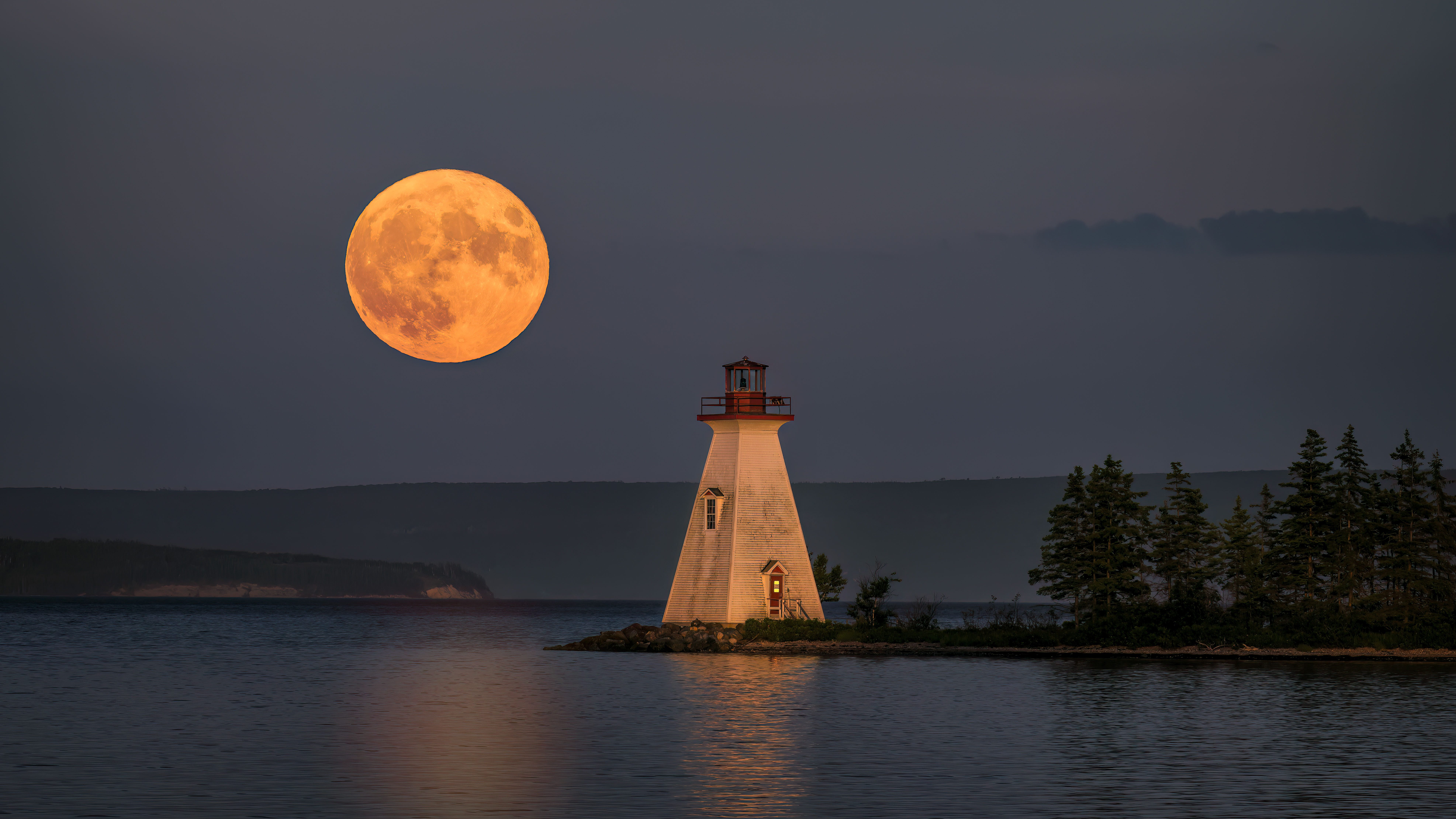 The July 2022 Supermoon rises near the Kidston Island Lighthouse on Kidston Island, located in the Bras d'Or lakes in Baddeck, Nova Scotia, Canada.  Kidston Island is an uninhabited island in the Bras d'Or Lakes in Baddeck, Nova Scotia.