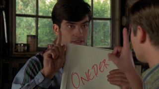 Johnathon Schaech gestures while showing the band's name on a note pad in That Thing You Do!