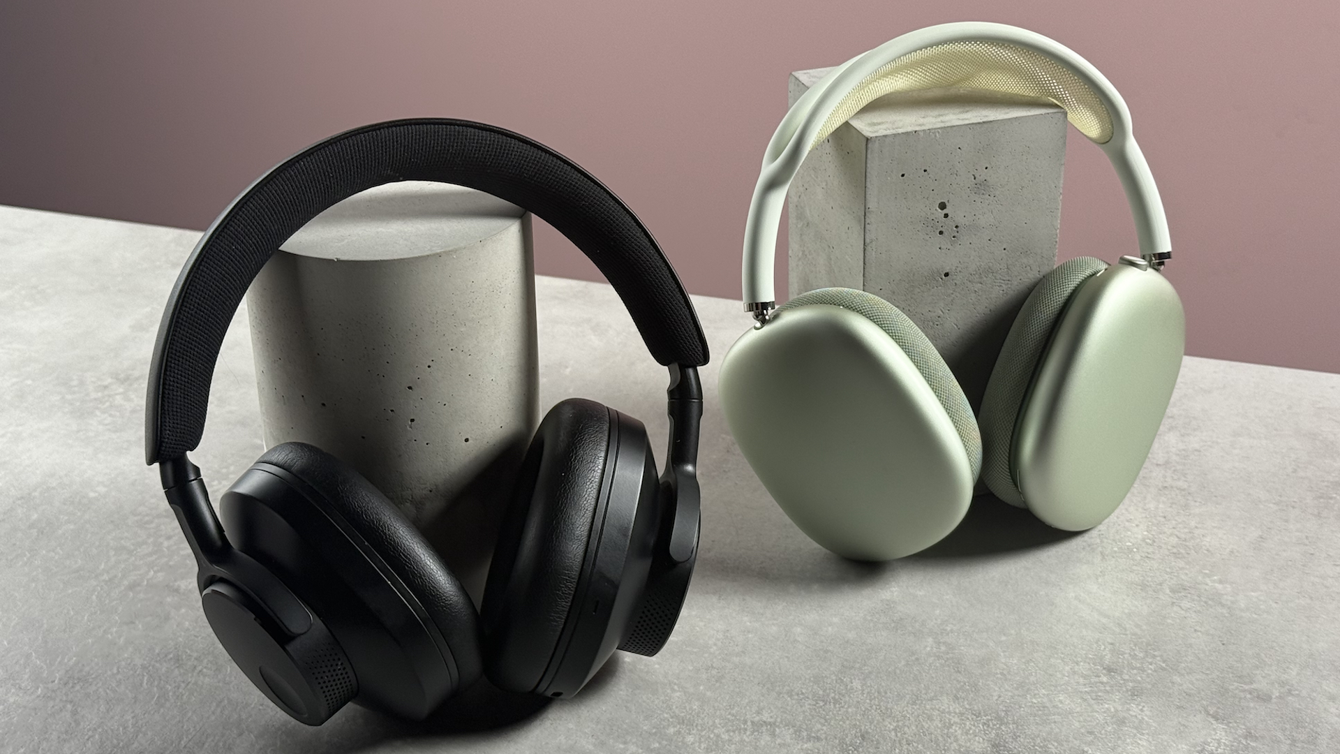 The Cambridge Audio Melomania P100 and AirPods Max at a 3/4s angle propped up in front of a pink background.