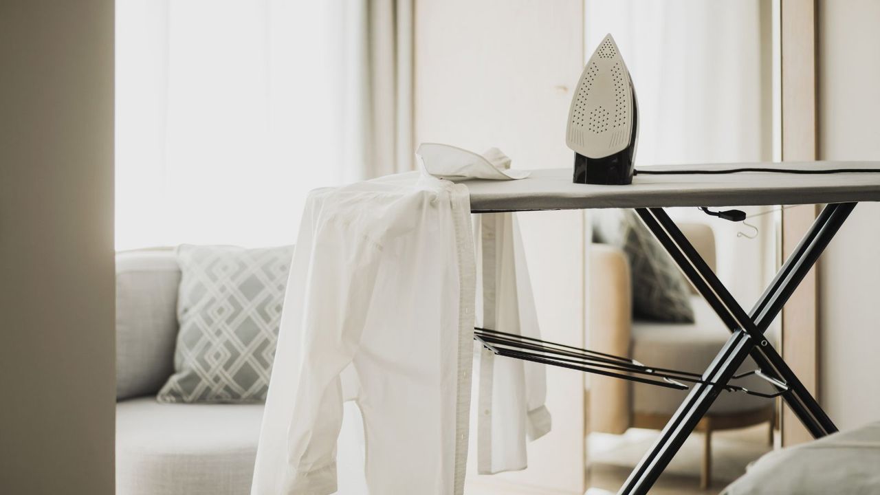 Interior of room with ironing board, electric iron and white shirt on ironing board.. Iron on the ironing board. 