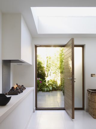 Horizontally paneled wood front door open to outside and hallway with white floor and fireplace