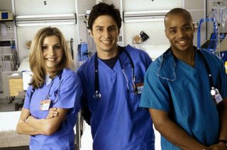 three doctors in blue scrubs at a hospital smiling in a promo shot for Scrubs