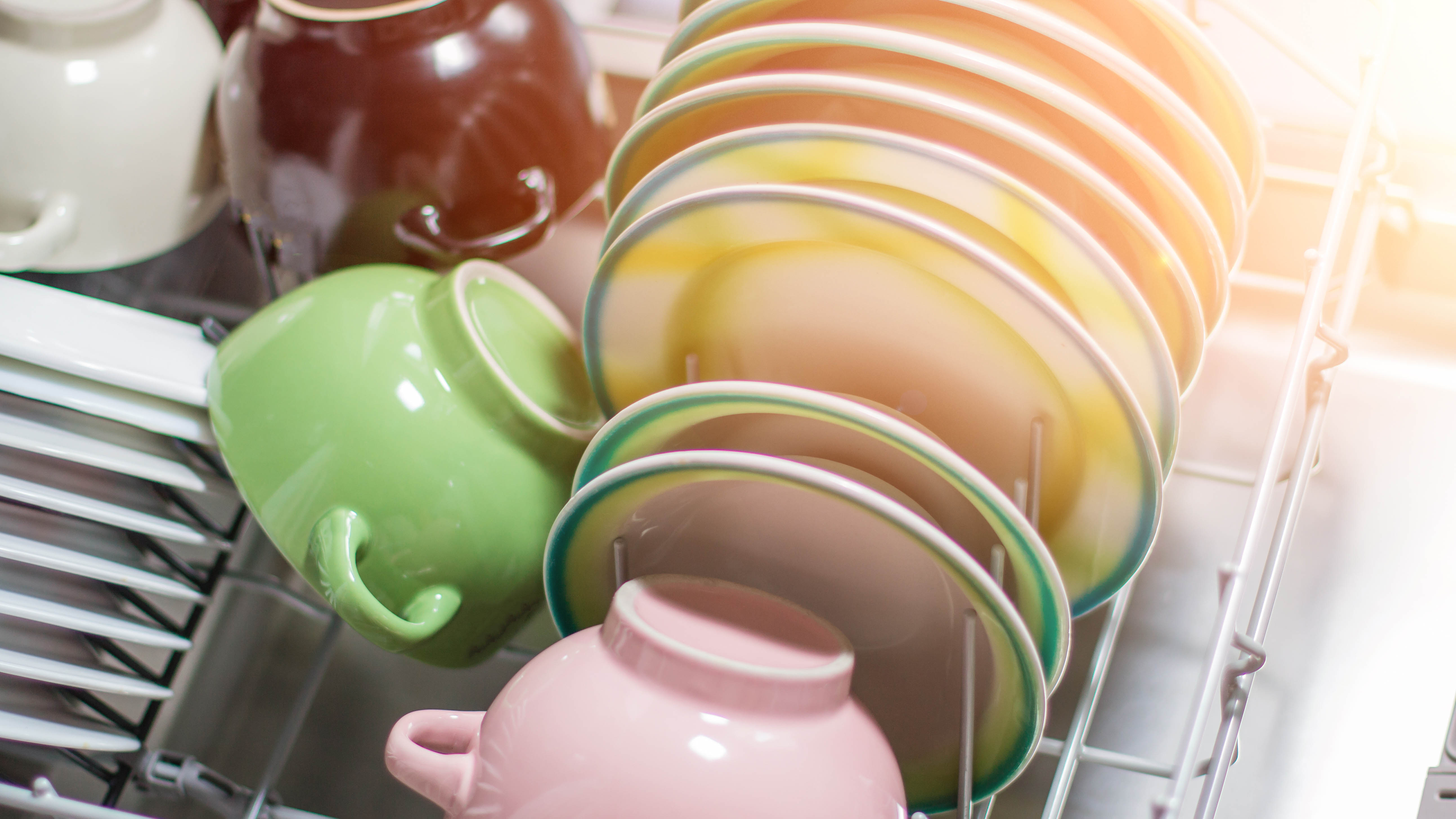 Посудомоечная машина, наполненная разноцветными тарелками и мисками