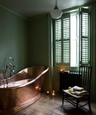 dark green shutters and walls in a bathroom with copper slipper bath