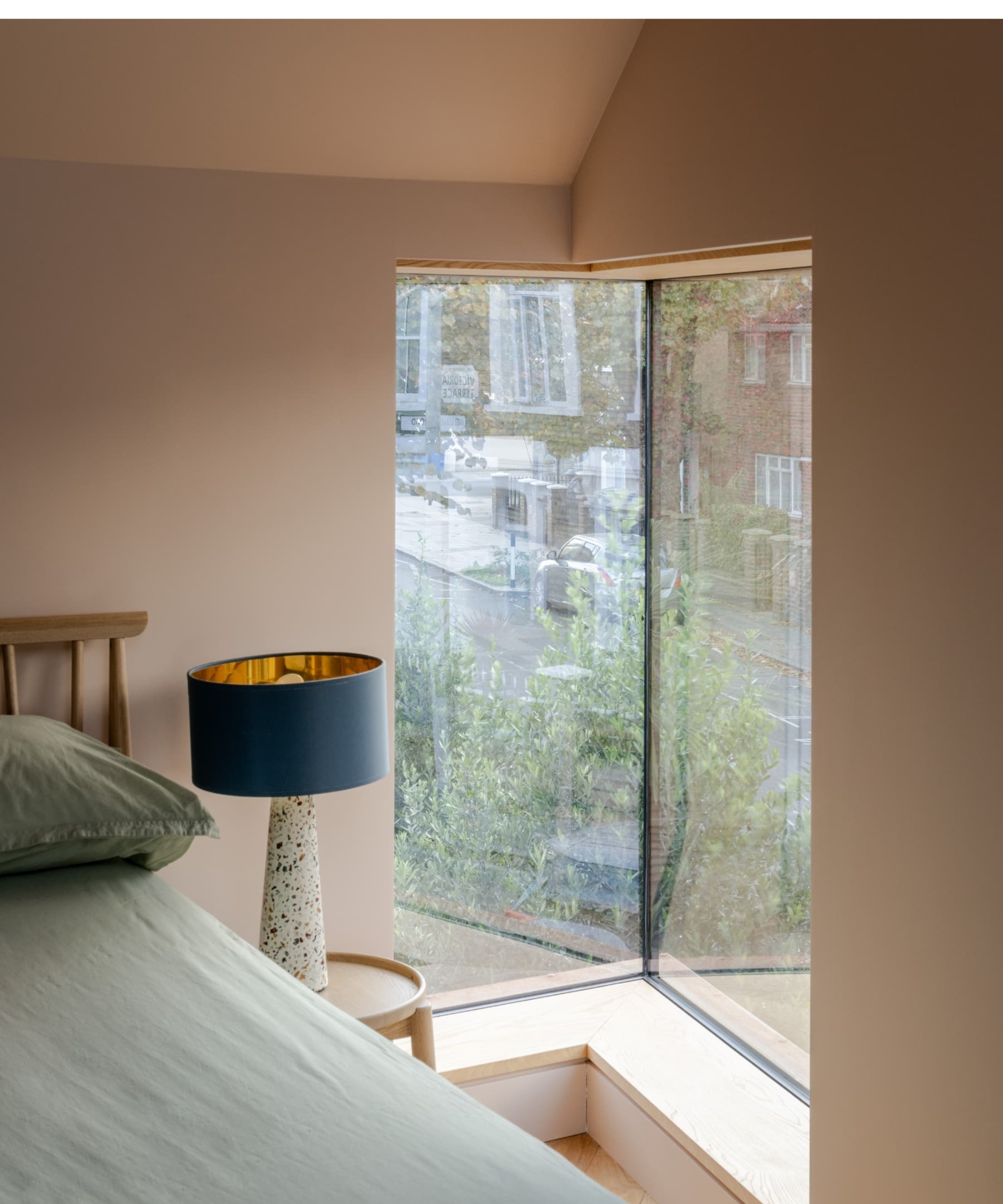 Frameless corner window in a bedroom, with a bed, lamp, and view over a residential street.