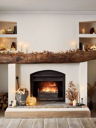 Garland on wooden mantle with fall colors and lit fireplace, pumpkins, candles and fire lit