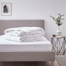 A folded duvet on a stripped bed with a side table
