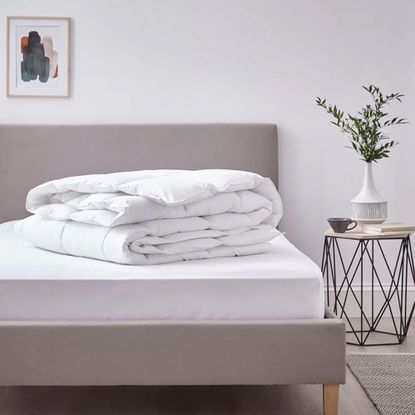 A folded duvet on a stripped bed with a side table