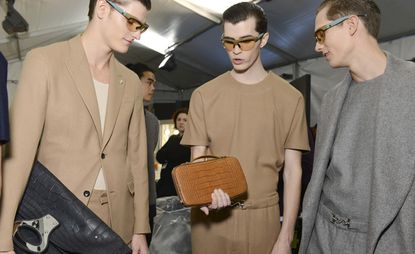 Male models wearing glasses, looking at a clutch bag