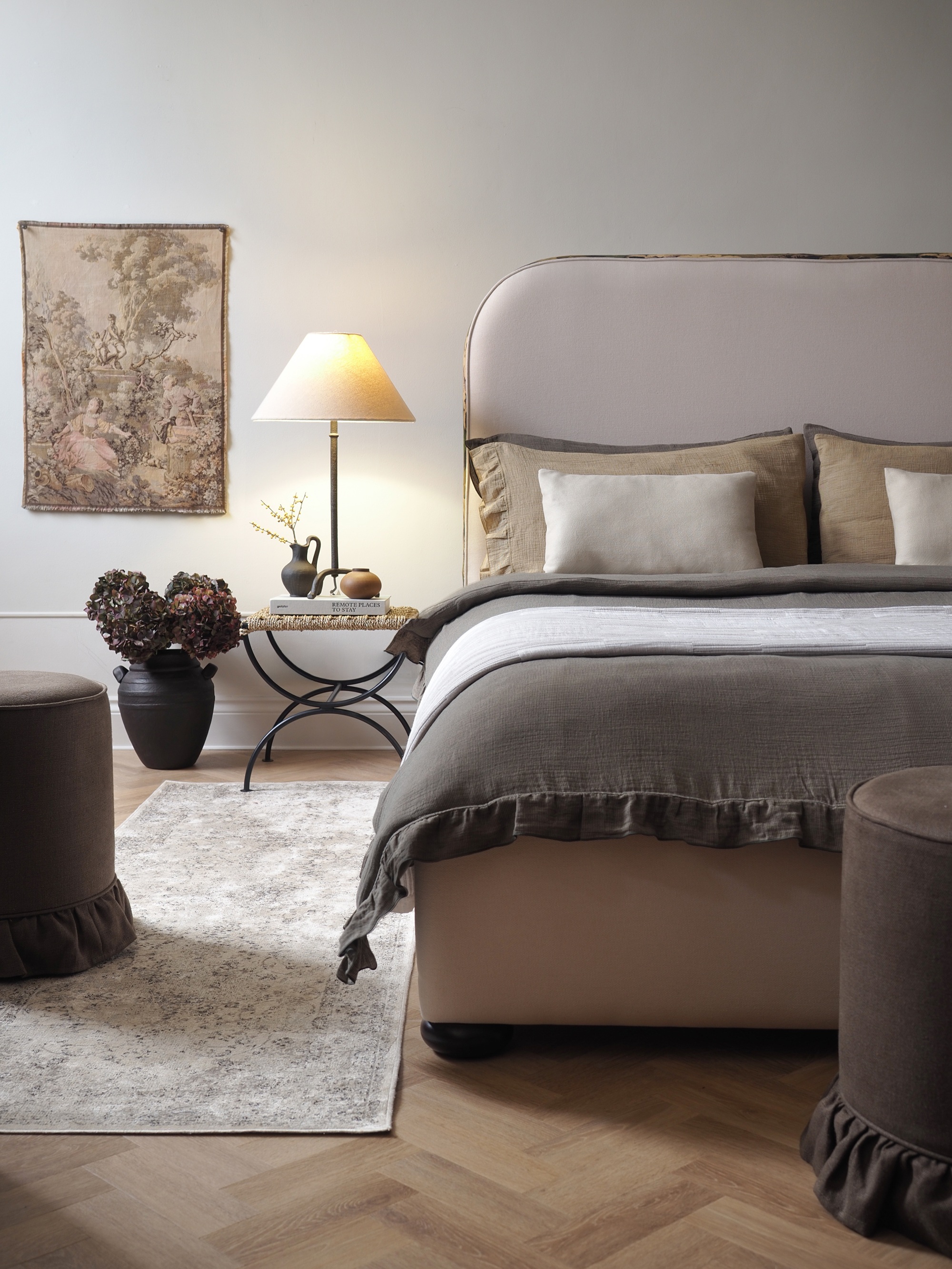 a bedroom with a traditional style, neutral bedding, a patterned vintage rug, and a table lamp lit