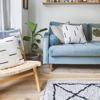 living room wood floor ideas, Scandi style living room with wood flooring, blue sofa, wood and rattan armchair, textured rug, plant, basket, shelf