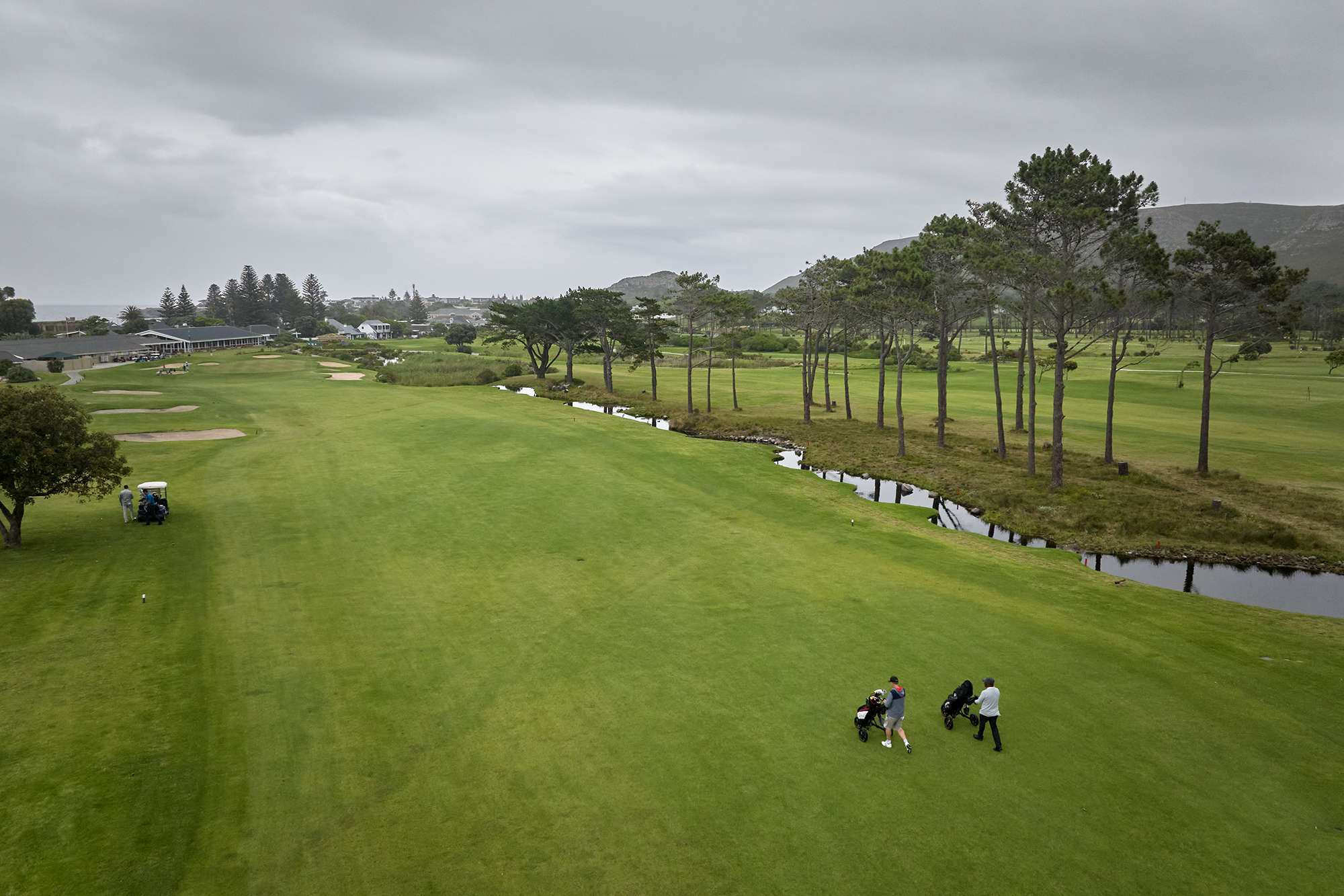 Two golfers walking on a golf course, on the fairway, with a golf buggy parked in the rough further up on the left