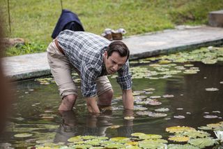 Neville (Ralf Little) stands in the pond at the Paradise Bary care home, with his trousers rolled up, crouching down with his forearms fishing around in the water
