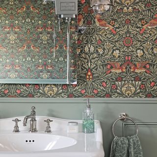 patterned wallpaper, green wall panelling, white sink with silver taps under mirror