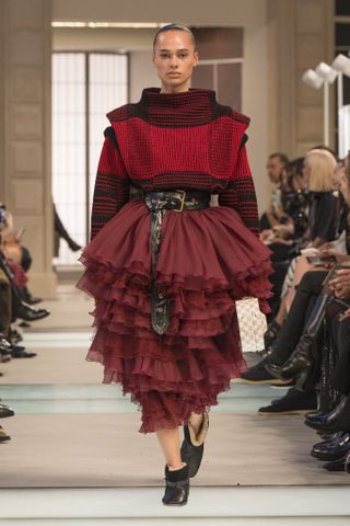 A model wearing a wide mock neck red plaid sweater with a belted, ruffled skirt at the F/W 25 Louis Vuitton show.