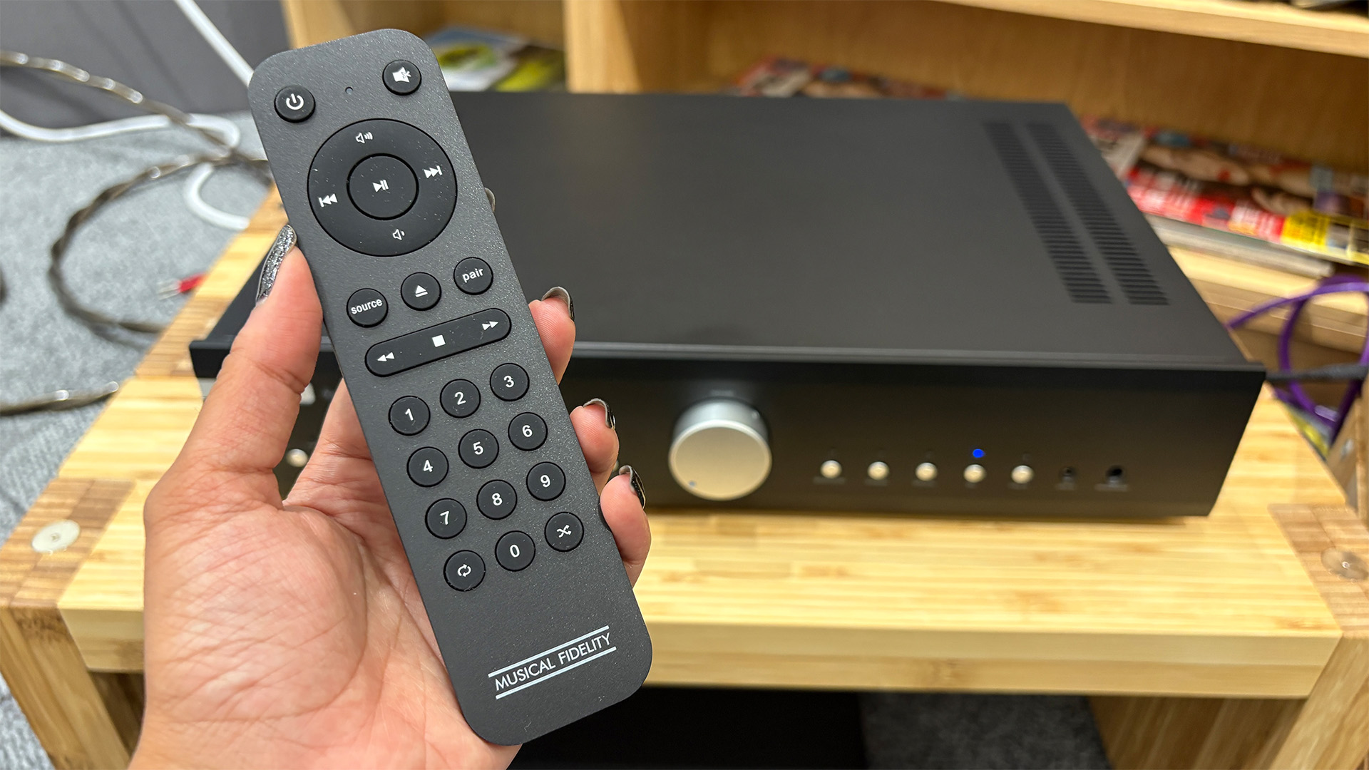 Musical Fidelity B1xi integrated amplifier on wooden hi-fi rack with remote control held in hand in front of i